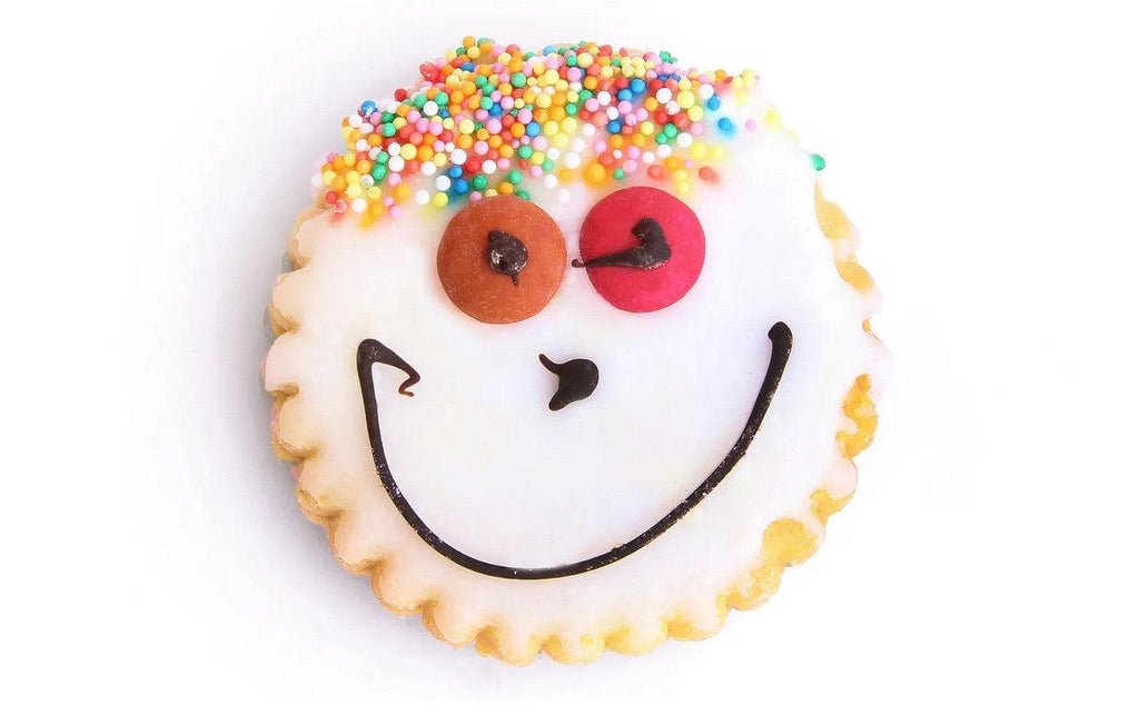 Funny Face Cookie round a topped with smarties, hundreds and thousands and chocolate drizzle